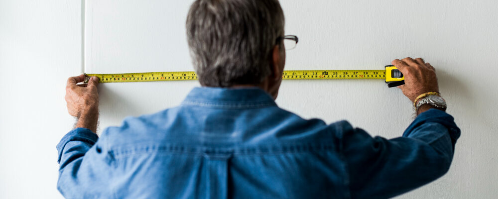 мужчина измеряет стену рулеткой