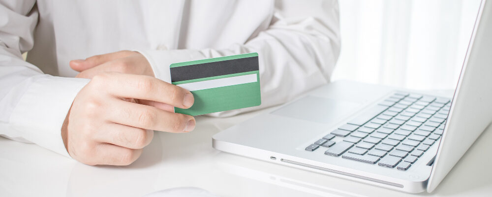 человек держит кредитную карточку перед ноутбуком